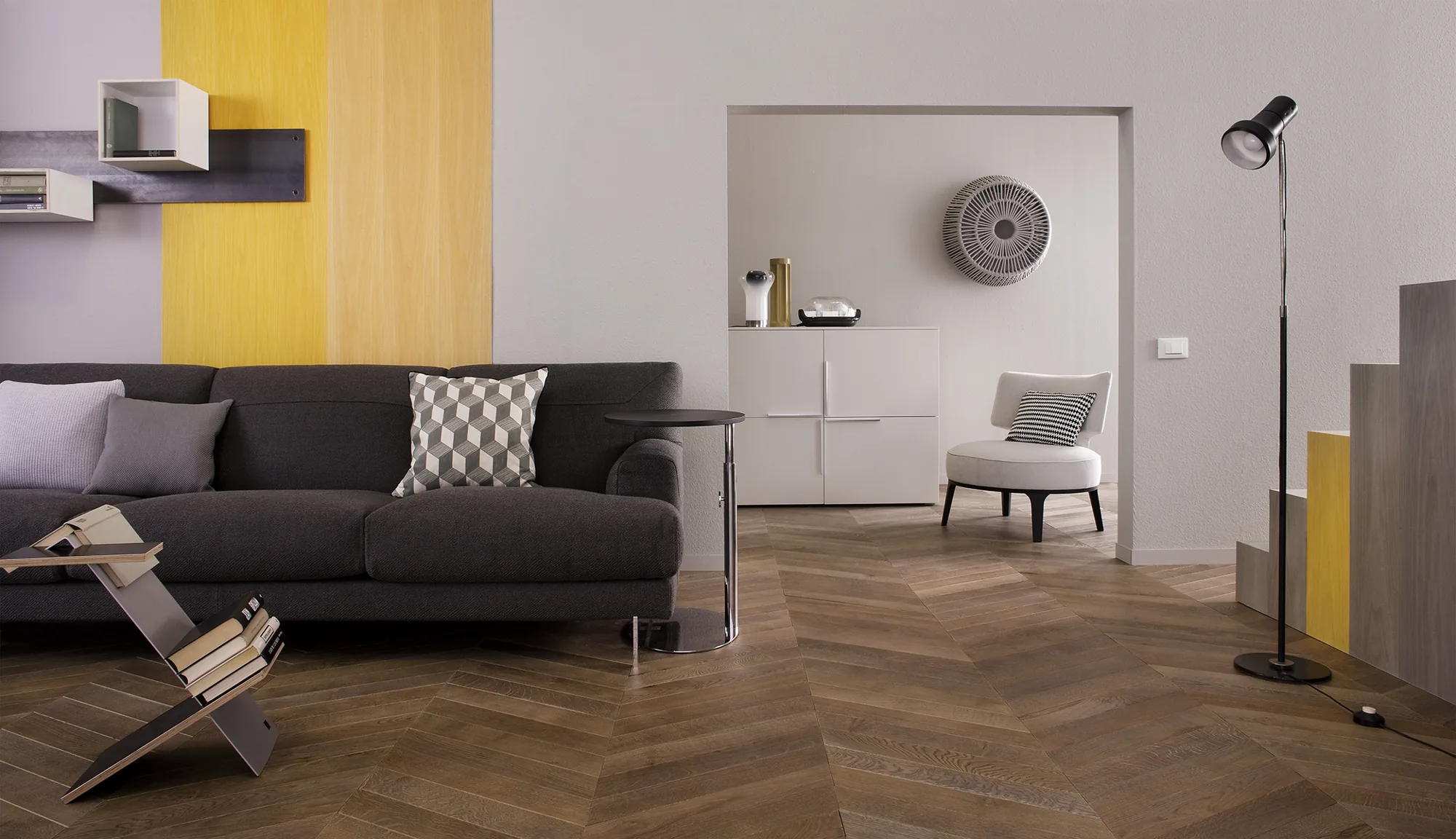 Living room with dark grey sofa, geometric cushion, herringbone parquet and yellow wall band, light armchair behind — photo Filippo Piantanida