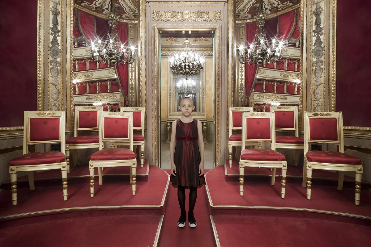 Bambina in abito rosso scuro tra sedie dorate in un palco rosso e oro del Teatro alla Scala — Filippo Piantanida e Roberto Prosdocimo