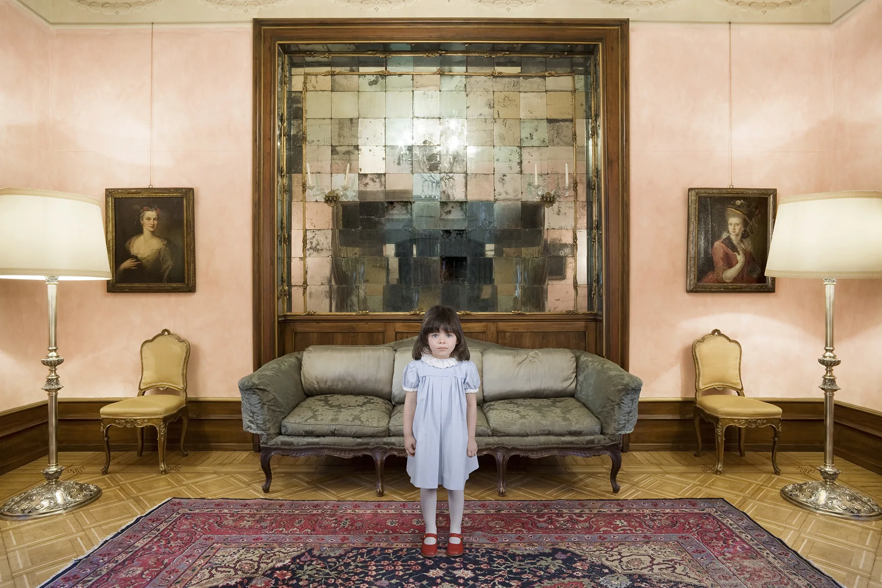 Bambina in abito azzurro al centro di un salotto rosa con specchio antico, divano e ritratti d'epoca — Filippo Piantanida e Roberto Prosdocimo
