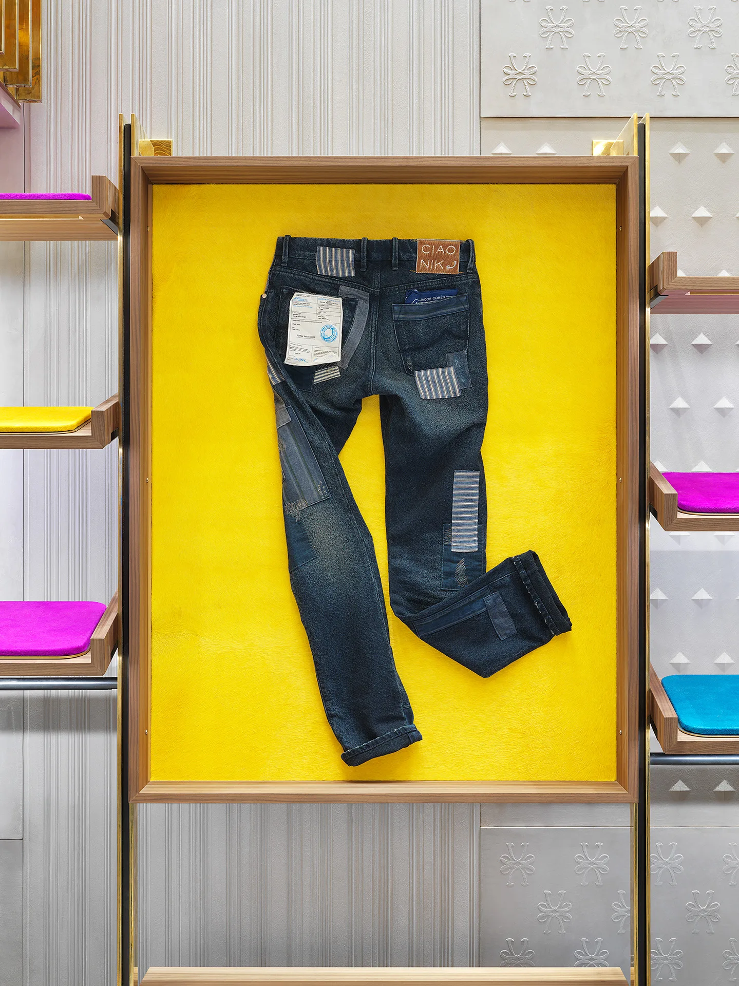 Jacob Cohën jeans with "CIAO NIK" label framed on yellow pony-hair ground, shelves with fuchsia and blue cushions — photo Filippo Piantanida Studio