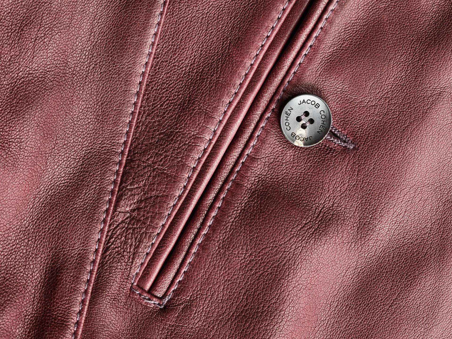 Macro of a Jacob Cohen burgundy leather jacket with an engraved metal button and contrast stitching — product still life, Filippo Piantanida Studio