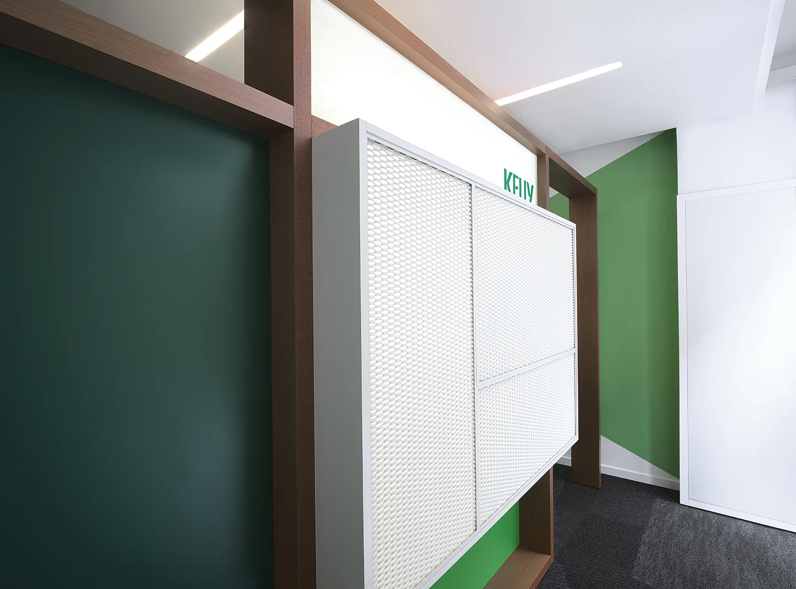 Dettaglio Kelly Hub: pannello in rete metallica bianca con logo verde su struttura in legno, pareti verde scuro e moquette grigia — foto Filippo Piantanida