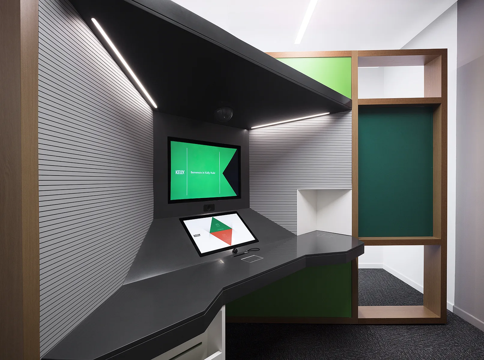 Cabina self-service Kelly Hub con schermo verde, monitor touch e soffitto nero a fascia luminosa, nicchie verdi e legno — foto Filippo Piantanida