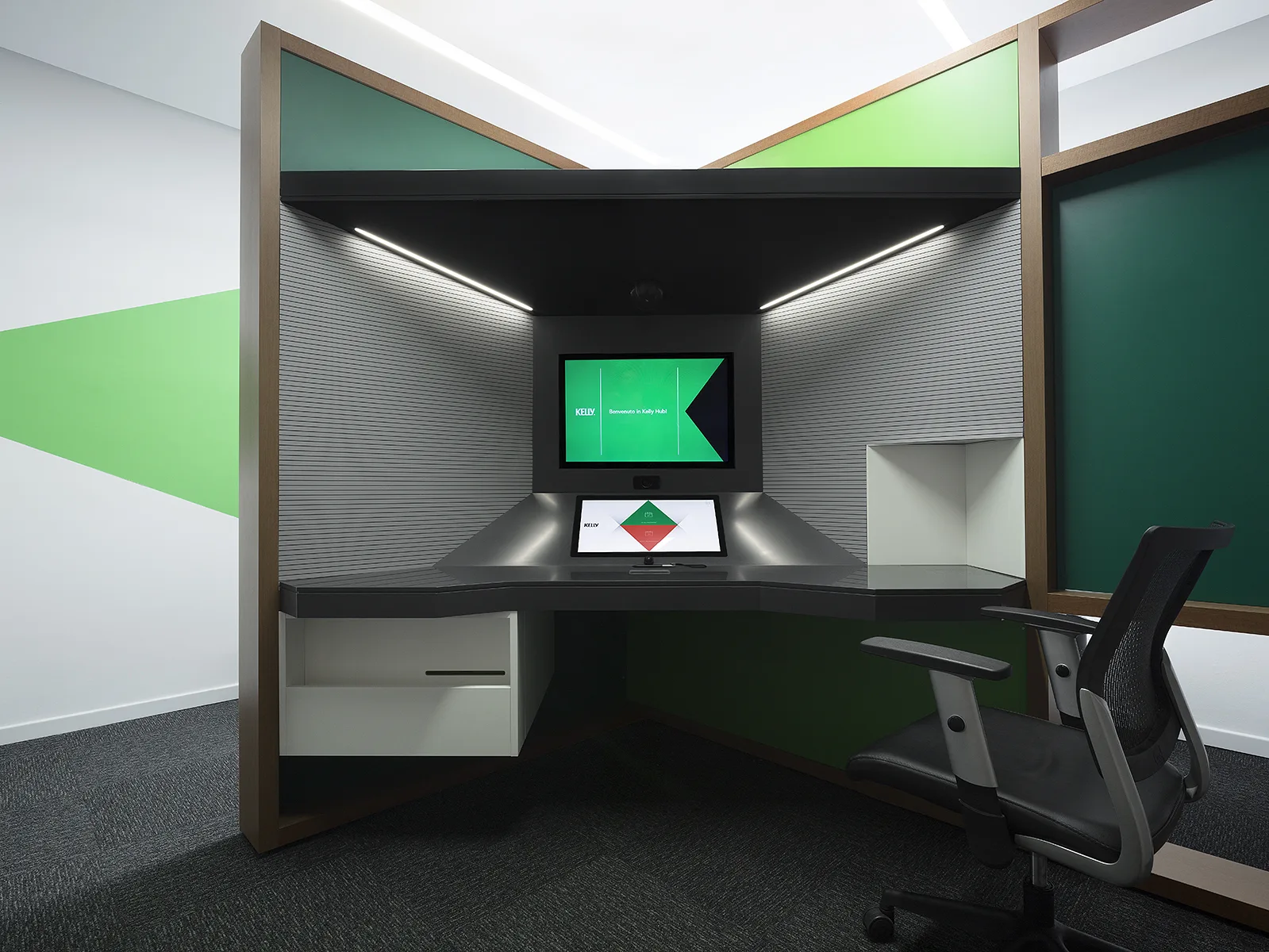 Postazione Kelly Hub con sedia operativa nera, schermo di benvenuto verde, piano antracite e struttura in legno con nicchie verdi — foto Filippo Piantanida
