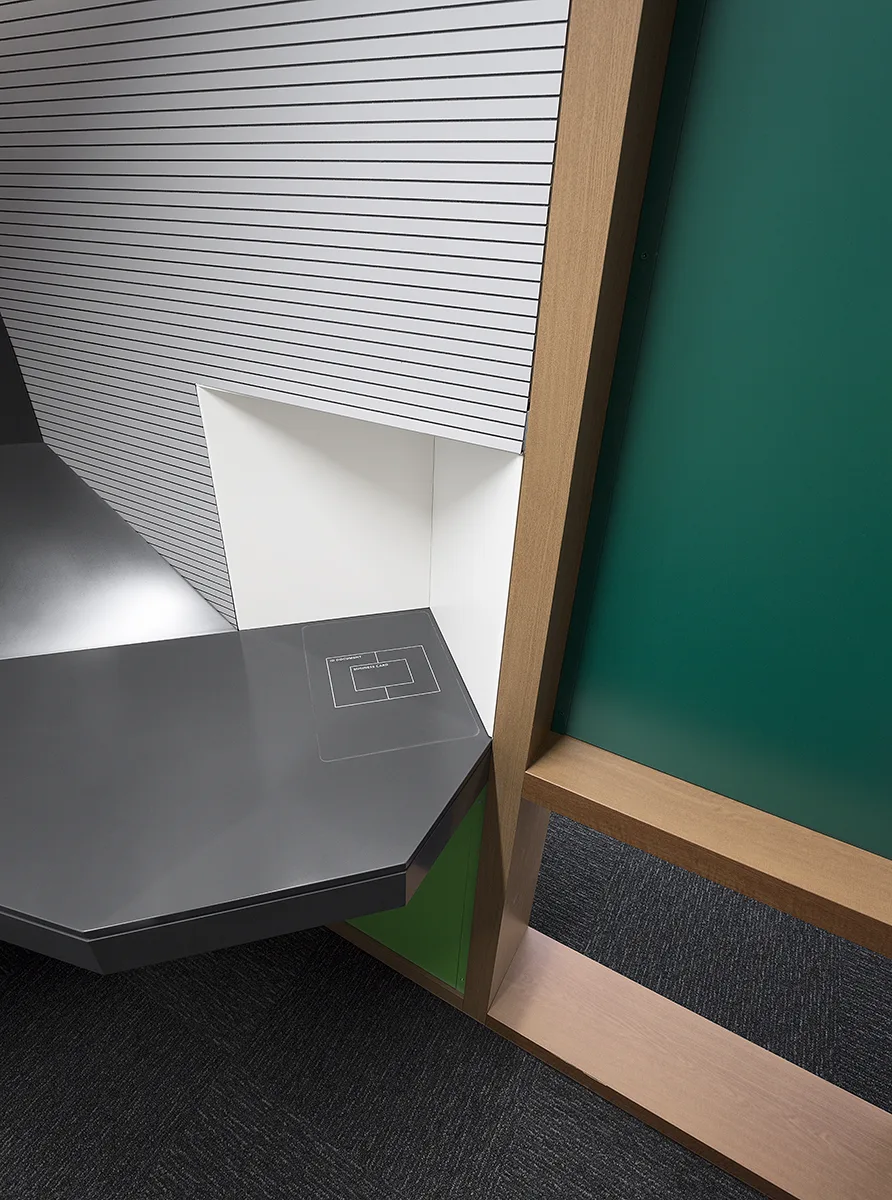 Dettaglio architettonico della postazione Kelly Hub: piano antracite, parete a doghe grigie, montante in legno e parete verde — foto Filippo Piantanida