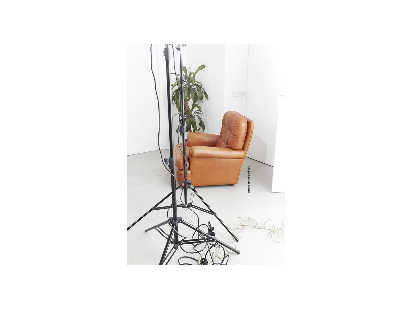 Behind the scenes of a photo shoot: tan leather armchair and studio lights on a minimal white background.